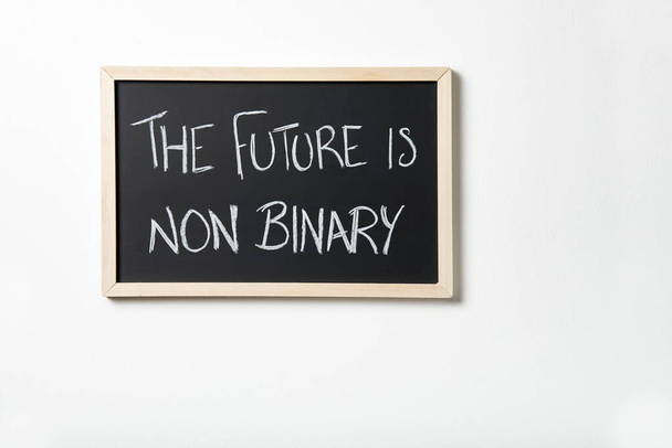 Blackboard lóg egy fehér falon a szöveggel A jövő nem bináris van ráírva krétával. A nemek közötti sokféleség tiszteletben tartásának fogalma. - Fotó, kép