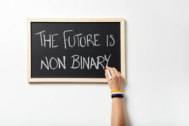 Mano con brazalete simbólico que marca el texto El futuro no es binario en una pizarra. Concepto de respeto a la diversidad de género. - Foto, Imagen