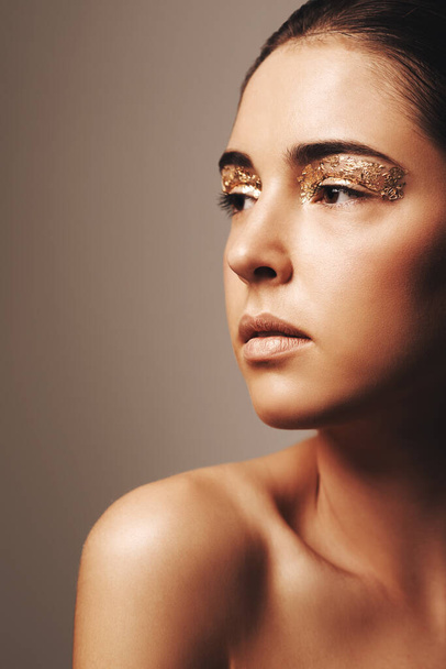Gorgeous and golden. Studio shot of an attractive brunette wearing gold make up and looking away. - Zdjęcie, obraz