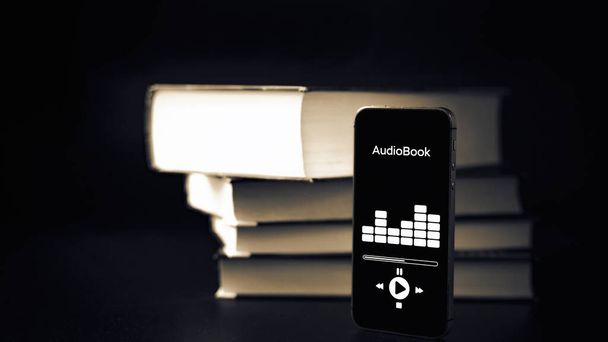Audiobook education. Smartphone screen with audiobook application on paper books black background. Ebook e learning electronic internet mobility concept - Photo, Image