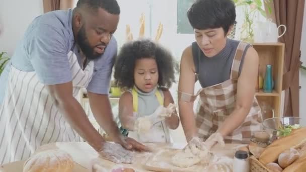 Familia afroamericana con harina de trilla hija para cocinar con el padre y la madre juntos en la cocina en casa, padres e hijos pequeños preparando la comida con diversión, relación y actividad. - Imágenes, Vídeo