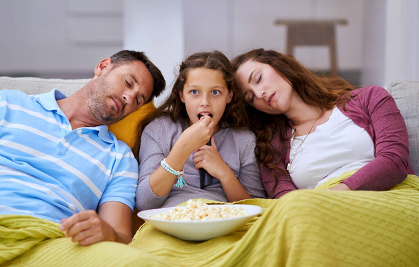 Movie night ran too long for her parents. Cropped shot of a young girl watching a movie while both her parents sleep on either side of her. - 写真・画像