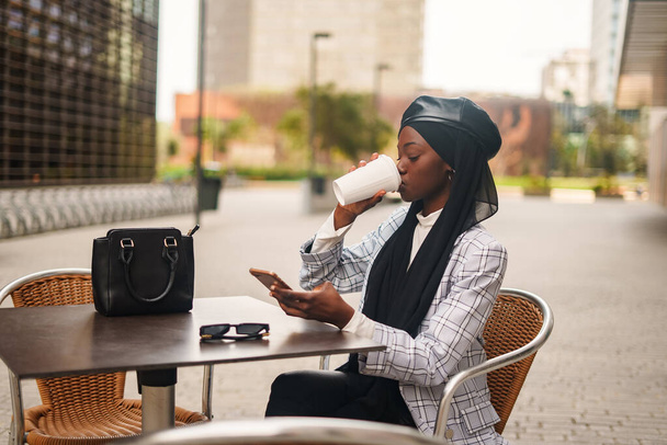 黒のエレガントな女性はコーヒーを飲み、スマートフォンを閲覧 - 写真・画像