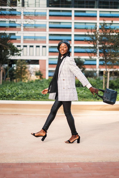 Vrolijke zwarte dame in stijlvolle kleding wandelen in het stadspark - Foto, afbeelding