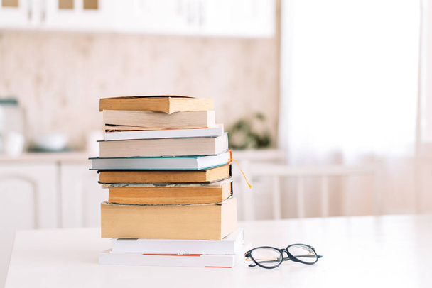 Stack of books with glasses standing on a table in front of the kitchen - Photo, Image