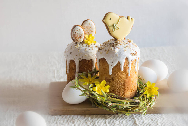Traditional easter cake decorated with easter cookies, willow twigs in shape of nest, yellow flowers, white eggs on linen tablecloth. Side view, selective focus. Easter treat, holiday symbol - Foto, Imagem