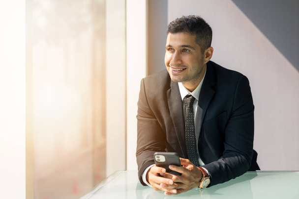 Business portrait of caucasian businessman in business suit holding mobile phone on hand at workplace indoor - Photo, image