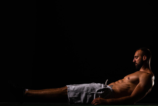 Yakışıklı ve üstsüz adam yerde yatarken karın kaslarını çalıştırıyor. - Fotoğraf, Görsel