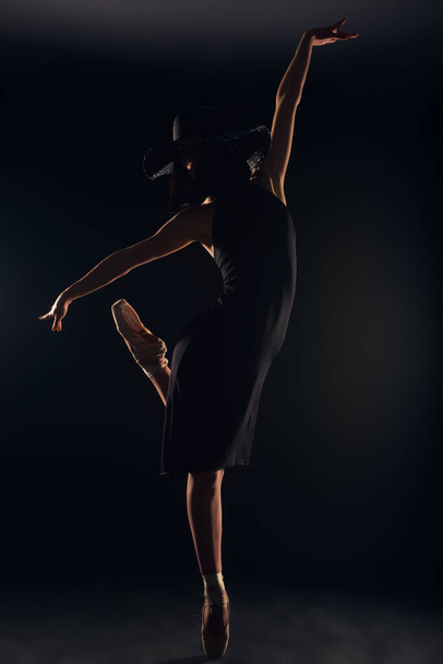 Muchacha atractiva está en sus zapatos de punto, mientras que el vestido en vestido negro y sombrero negro en el estudio - Foto, imagen
