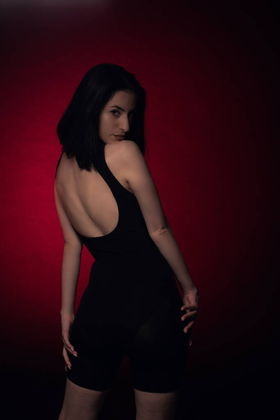 Menina sedutora está posando a partir das costas no fundo vermelho no estúdio - Foto, Imagem