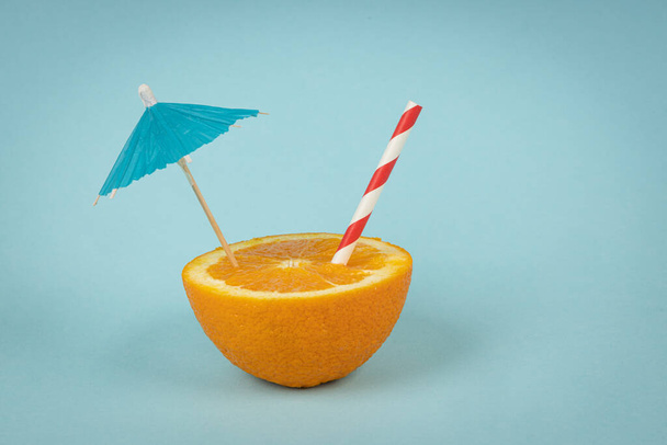 Orange cut in half with straw and umbrella on blue background. Summer concept.  - Fotoğraf, Görsel