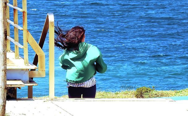 Brunette en collants avec chemisier vert prenant des photos par l'océan - Photo, image