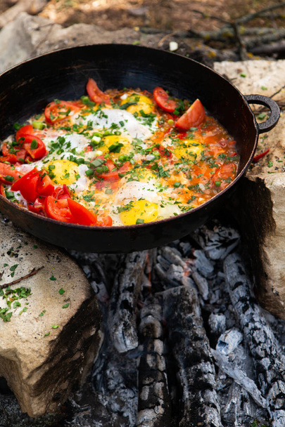 Los huevos preparados con verduras en una sartén en el fuego en el bosque. Cocinar huevos revueltos sobre un fuego abierto. Desayuno en la naturaleza. Comida turística. - Foto, Imagen