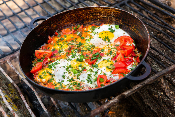Яйца, приготовленные из овощей на сковороде в лесу. Готовить яичницу на открытом огне. Завтрак в природе. Туристическая еда. - Фото, изображение