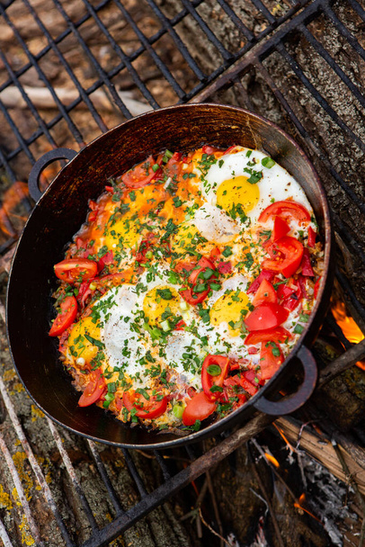 Jaja przygotowane z warzyw na patelni na ognisku w lesie. Gotowanie jajecznicy na otwartym ogniu. Śniadanie w naturze. Żywność turystyczna. - Zdjęcie, obraz
