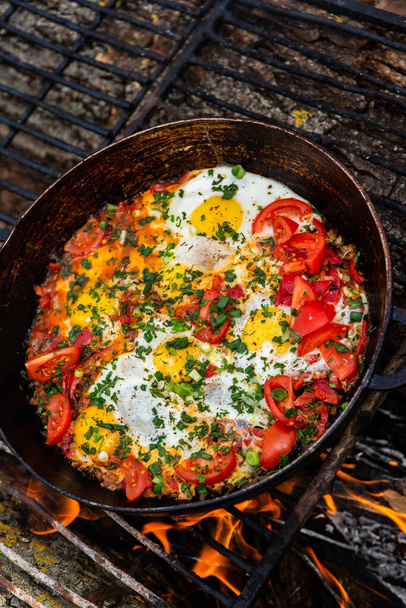 Los huevos preparados con verduras en una sartén en el fuego en el bosque. Cocinar huevos revueltos sobre un fuego abierto. Desayuno en la naturaleza. Comida turística. - Foto, imagen