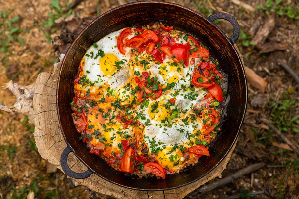 Αυγά που παρασκευάζονται με λαχανικά σε ένα τηγάνι στη φωτιά στο δάσος. Μαγειρεύοντας ομελέτα πάνω από μια ανοιχτή φωτιά. Πρωινό στη φύση. Τουριστικά τρόφιμα. - Φωτογραφία, εικόνα