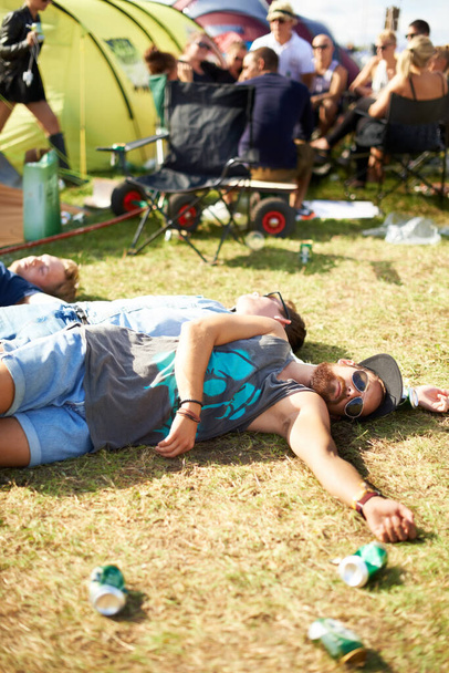 Cuando los buenos tiempos van mal. Tiro de un grupo de chicos desmayados en la hierba rodeados de latas de cerveza vacías en un festival al aire libre. - Foto, Imagen