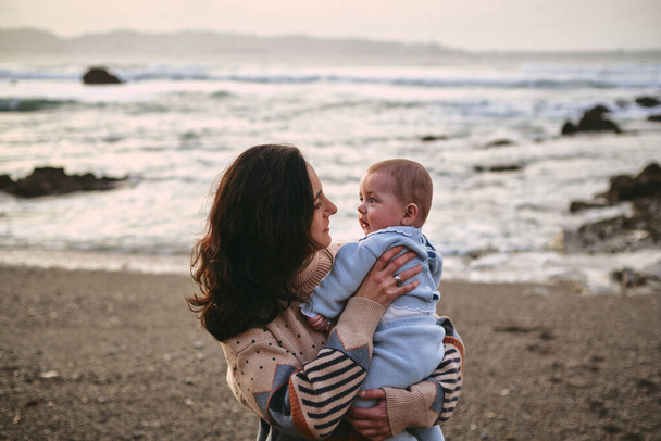 Одинока молода мати тримає і дивиться на свою дитину на пляжі
 - Фото, зображення