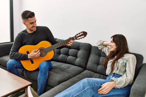 若いですヒスパニックカップル遊びスペイン語ギター座っていますザソファに家. - 写真・画像