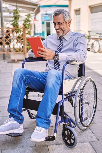 Moyen Age hispanique homme assis sur fauteuil roulant en utilisant touchpad à la rue - Photo, image