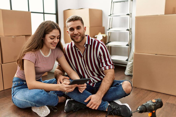 Junges kaukasisches Paar lächelt glücklich mit Smartphone im neuen Zuhause. - Foto, Bild