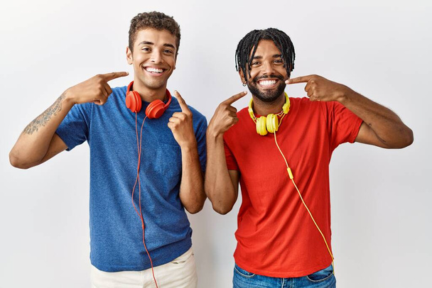 Young hispanic brothers standing over isolated background wearing headphones smiling cheerful showing and pointing with fingers teeth and mouth. dental health concept.  - Foto, afbeelding