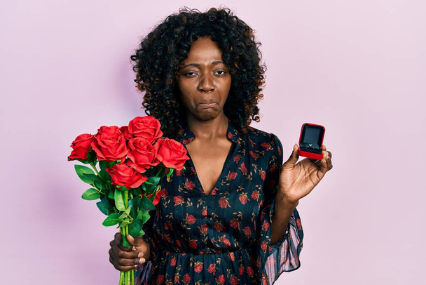 Junge afrikanisch-amerikanische Frau hält Blumenstrauß und Verlobungsring deprimiert in der Hand und macht sich Sorgen vor Kummer, weint wütend und ängstlich. Traurige Miene.  - Foto, Bild