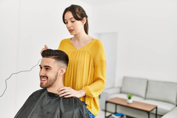 Молодая латиноамериканская парикмахерша стрижет мужские волосы электрической бритвой в салоне красоты. - Фото, изображение