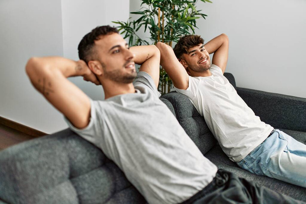 Deux hommes hispaniques couple souriant confiant détendu avec les mains sur la tête à la maison - Photo, image