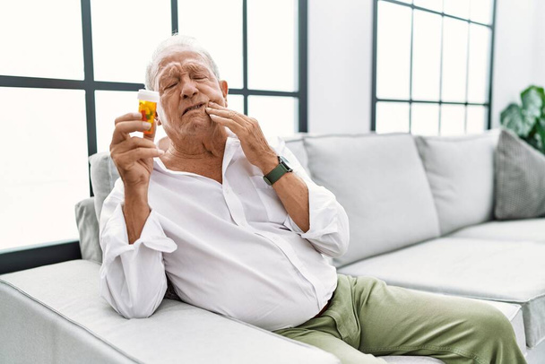 Senior man holding pills touching mouth with hand with painful expression because of toothache or dental illness on teeth. dentist concept.  - Фото, изображение