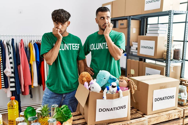 Young gay couple wearing volunteer t shirt at donations stand looking stressed and nervous with hands on mouth biting nails. anxiety problem.  - Photo, Image