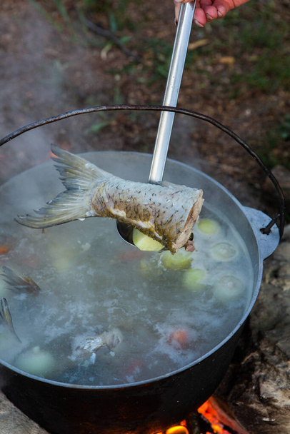 Fish soup prepared over an open fire. Cooking fish soup over an open fire in a kettle. Cooking in hiking tourism and fishing - Photo, Image