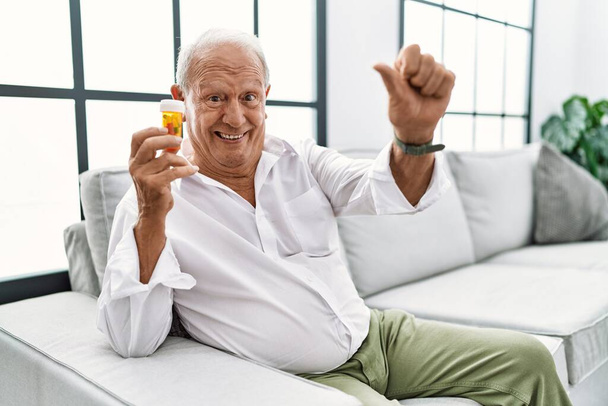 Hombre mayor sosteniendo pastillas aprobando hacer gesto positivo con la mano, pulgares arriba sonriendo y feliz por el éxito. gesto ganador.  - Foto, imagen