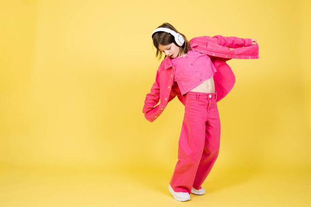Full body portrait of cute little girl dancing and listening to music on headphones isolated on yellow background - Φωτογραφία, εικόνα