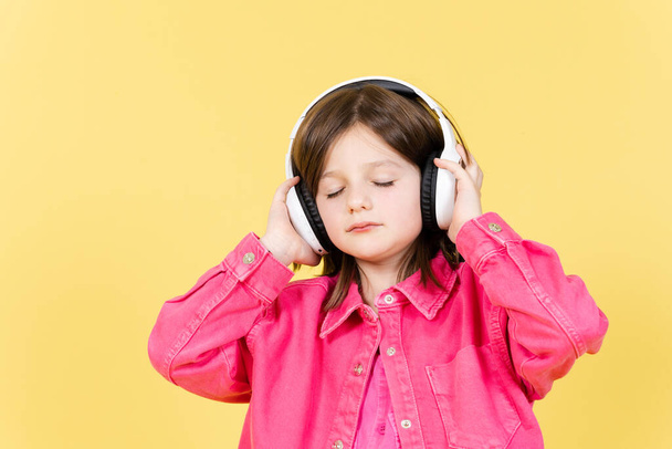 Roztomilé holčička poslech relaxační hudbu se zavřenýma očima na sluchátka izolované na žlutém pozadí - Fotografie, Obrázek