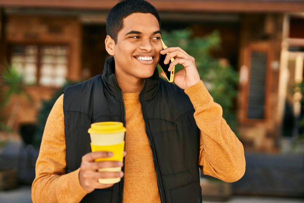 Nuori latinomies puhuu älypuhelimella ja juo kahvia kaupungissa - Valokuva, kuva