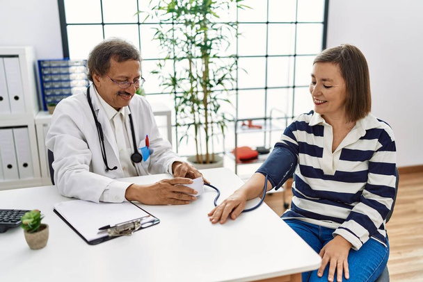 Middle age man and woman wearing doctor uniform having medical consultation auscultating using stethoscope at clinic - Photo, Image