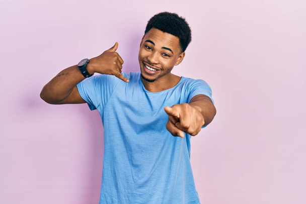 Young african american man wearing casual blue t shirt smiling doing talking on the telephone gesture and pointing to you. call me.  - Photo, Image