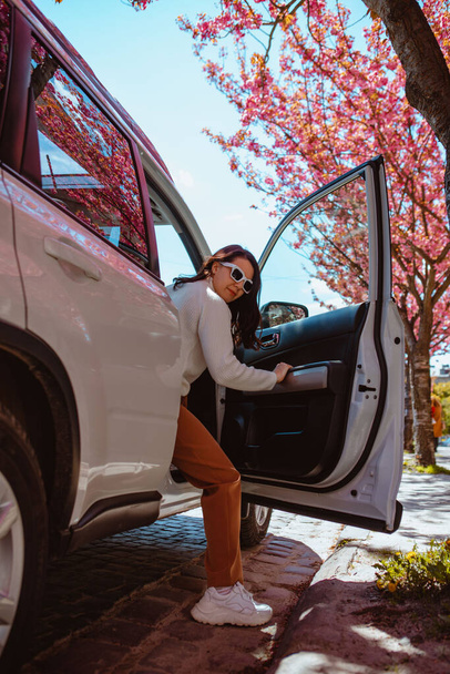 nő kiszáll az autóból virágzó sakura fa a háttérben másolás hely - Fotó, kép