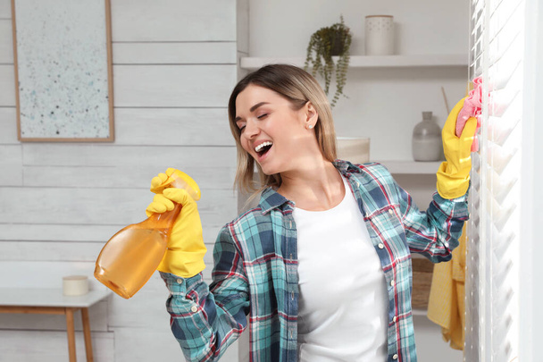 Woman with spray bottle and rag singing while cleaning at home - Foto, afbeelding