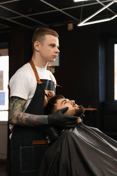 Professional hairdresser working with bearded client in barbershop - Photo, image