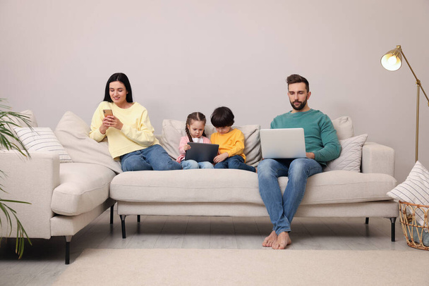 Happy family with gadgets on sofa in living room - Φωτογραφία, εικόνα