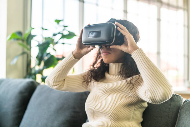 Donna latina utilizzando un auricolare realtà virtuale sul divano di casa - Foto, immagini