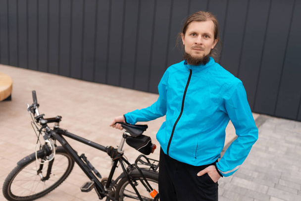 A man in a blue jacket is holding his bicycle and looking at the camera - Photo, Image