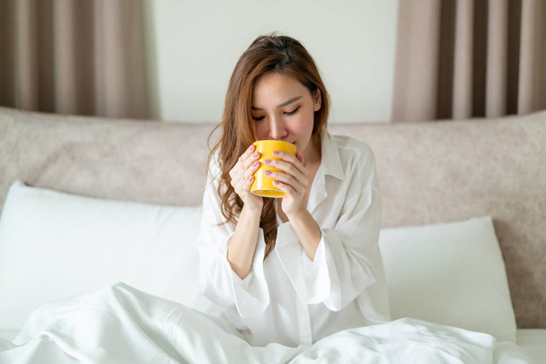 portrait beautiful Asian woman wake up and holding coffee cup or mug on bed in the morning - Fotografie, Obrázek