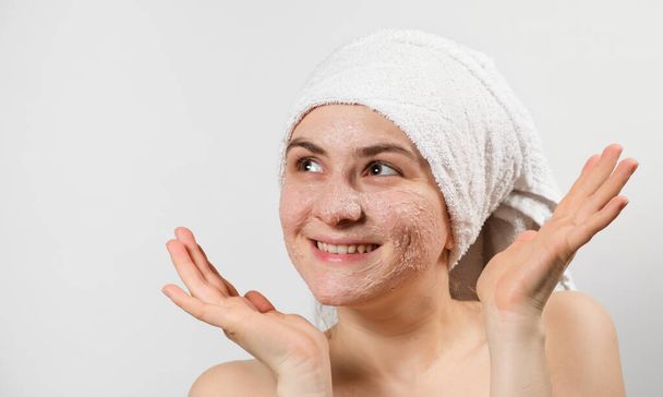 Μια όμορφη νεαρή γυναίκα εφάρμοσε ένα scrub ή μάσκα στο πρόσωπό της, περιποίηση προσώπου, καθαρισμό του δέρματος - Φωτογραφία, εικόνα