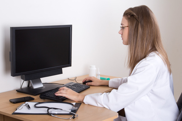 νεαρή γυναίκα γιατρός χρησιμοποιεί τον υπολογιστή με την κενή οθόνη  - Φωτογραφία, εικόνα