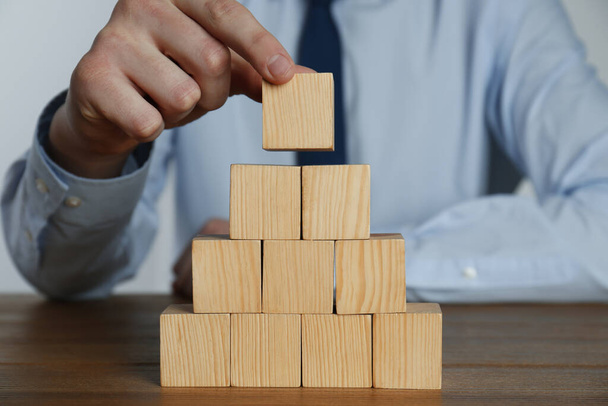 Businessman building pyramid of blank cubes on wooden table, closeup. Space for text - Photo, image
