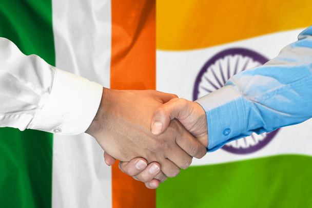 Negocios apretón de manos en el fondo de dos banderas. Hombres apretón de manos en el fondo de la bandera de Irlanda e India. Concepto de apoyo - Foto, imagen